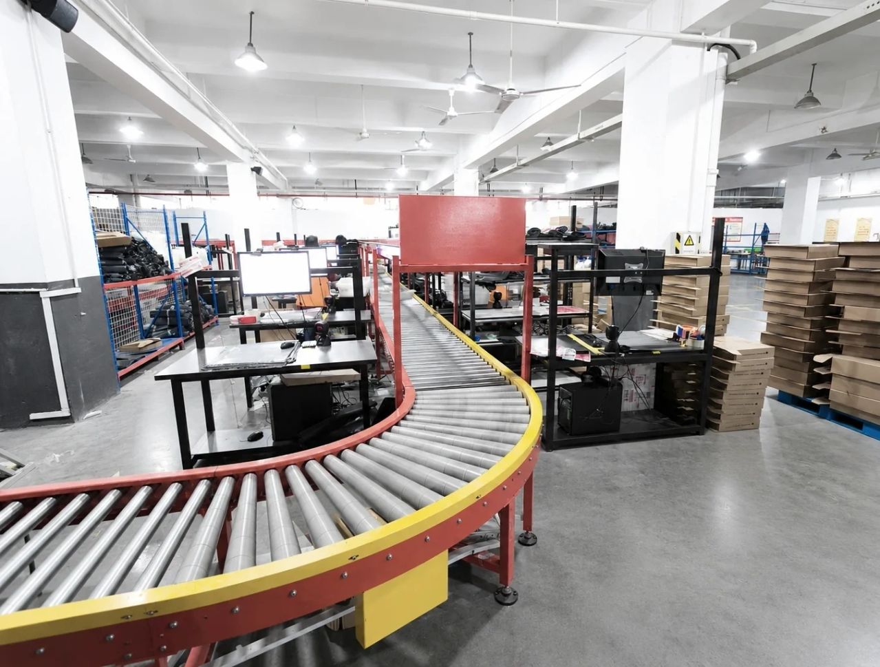 Curved roller conveyor through a warehouse packing floor, with benches, screens and stacked cartons