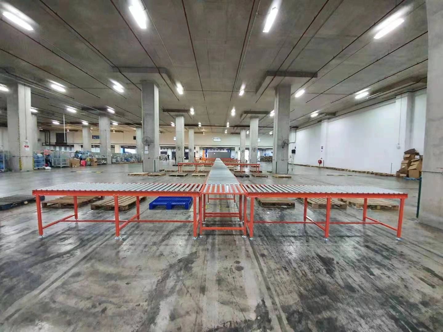 Roller conveyor line along a sorting floor, with a walk-through section for staff